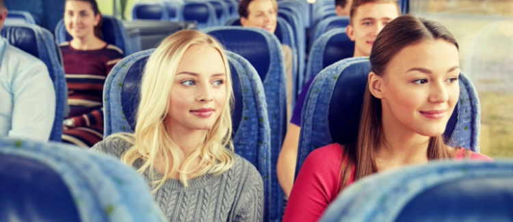 Två kvinnor sitter i en blå buss med andra personer i bakgrunden.