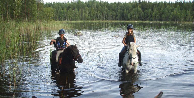 Ridande barn låter hästarna svalka sig i en sjö