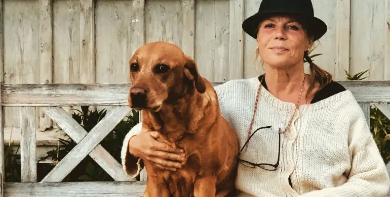 Bild på dam iklädd hatt tillsammans med en brun fin hund sittande på en bänk