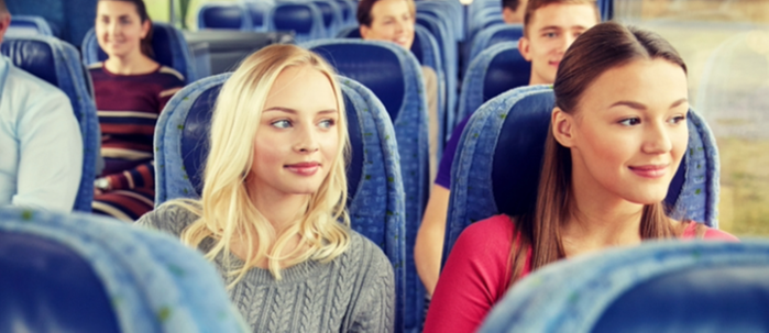 Två kvinnor sitter i en blå buss med andra personer i bakgrunden.